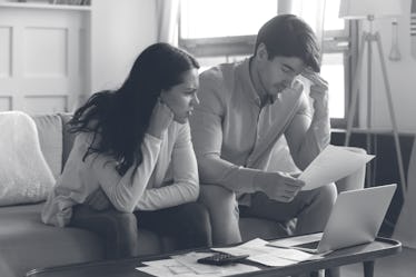 Falling behind with rent. Concerned worried young married couple sitting on sofa at home office stud...