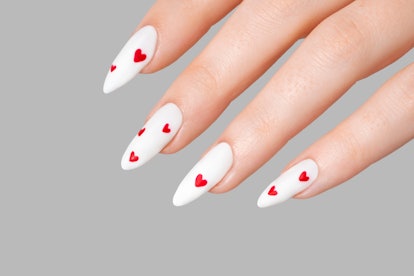 Female manicure one hand minimal gel polish white long nails and red hearts desing gray isolated bac...