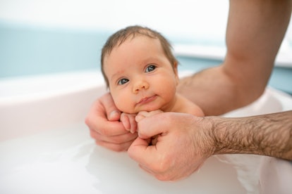 A baby takes a bath, held by their dad. There are lots of captions for baby's first bath to choose f...