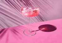 Pink champagne with ice on the table with sun shadows. On a pink background with palm leaves, front ...