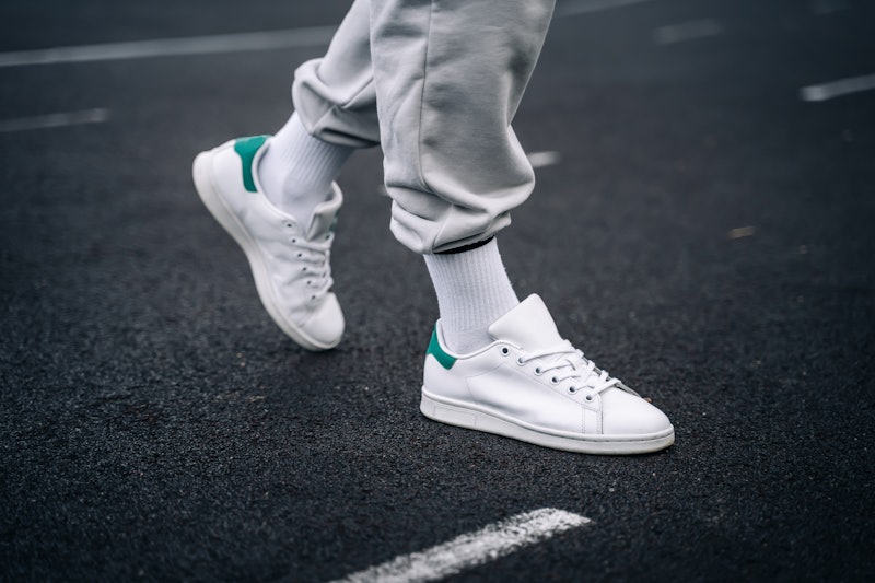 Women's legs in sweatpants, white socks and white sneakers with green elements against the backgroun...
