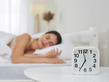 Close up of white plastic alarm clock set for 7 AM on bedside table in bedroom, with happy peaceful ...