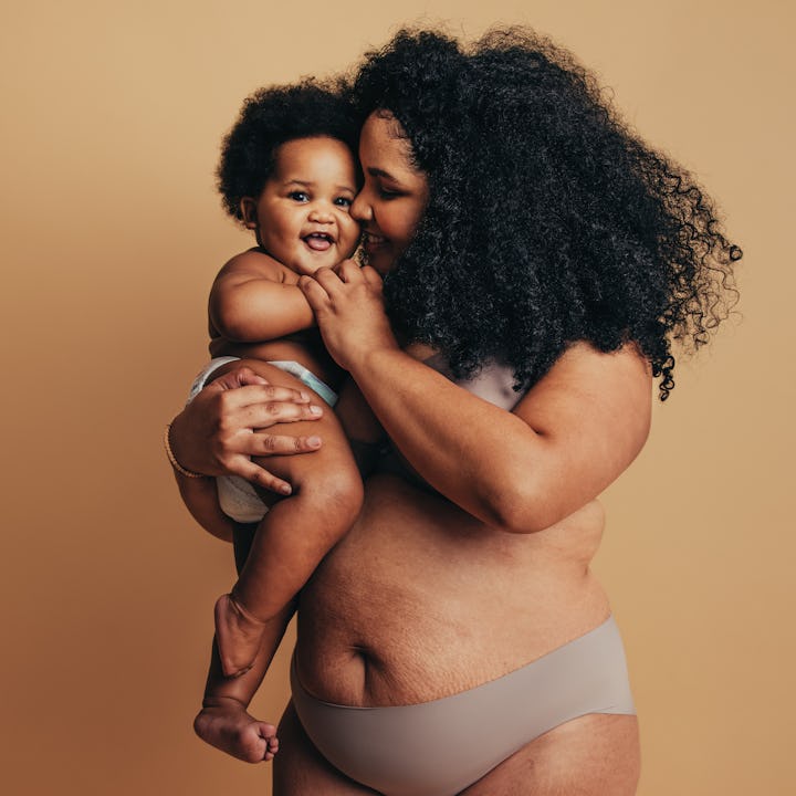 Loving mother with her baby against brown background. Happy woman carrying her toddler.