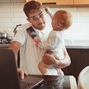 Multitasking father works from home while holding his baby.
