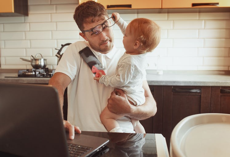 Multitasking father works from home while holding his baby.