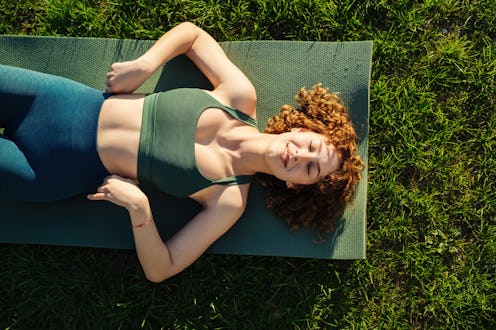 Top view of beautiful young happy sportive woman wearing green sports bra and blue yoga pant. Closed...