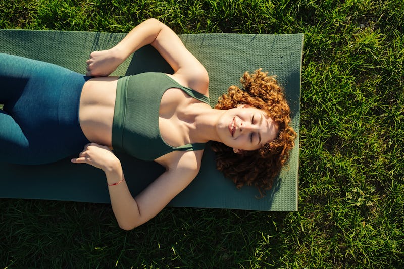 Top view of beautiful young happy sportive woman wearing green sports bra and blue yoga pant. Closed...