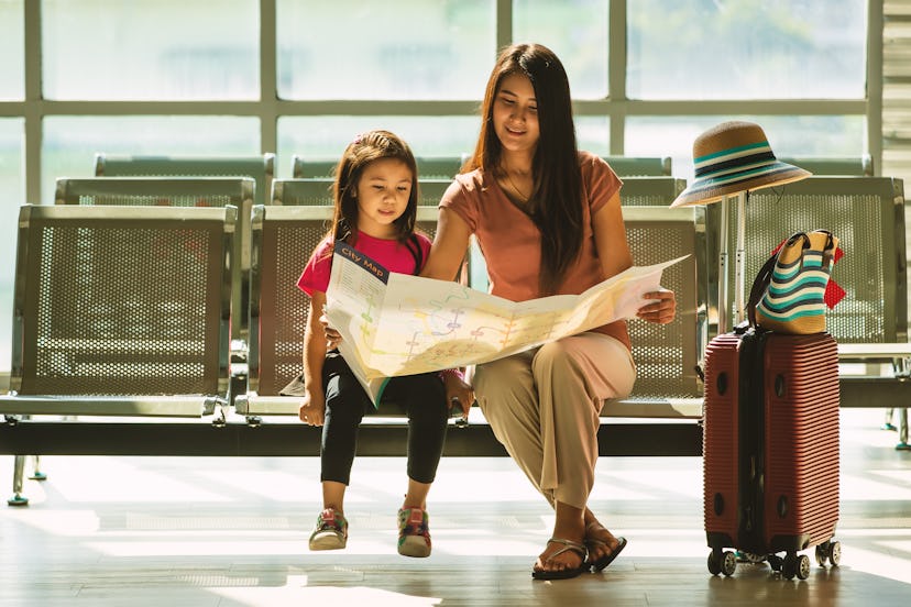 Asian mother and daughter traveler family sitting in airport terminal with social distancing signal ...