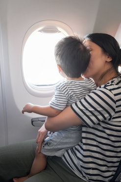Infant traveling in airplane sitting on its mother lap both looking out of an airplane window. One y...