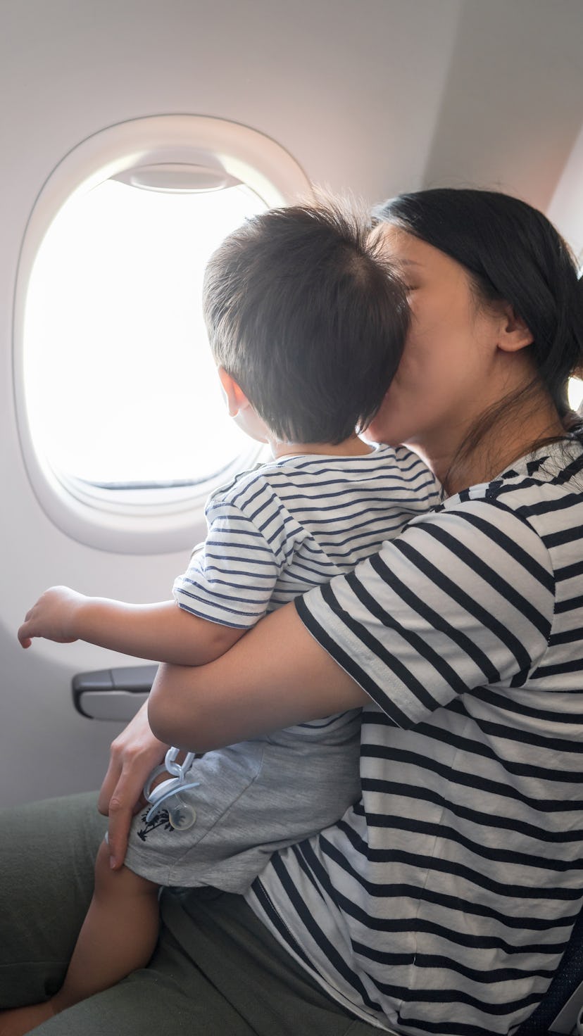 Infant traveling in airplane sitting on its mother lap both looking out of an airplane window. One y...