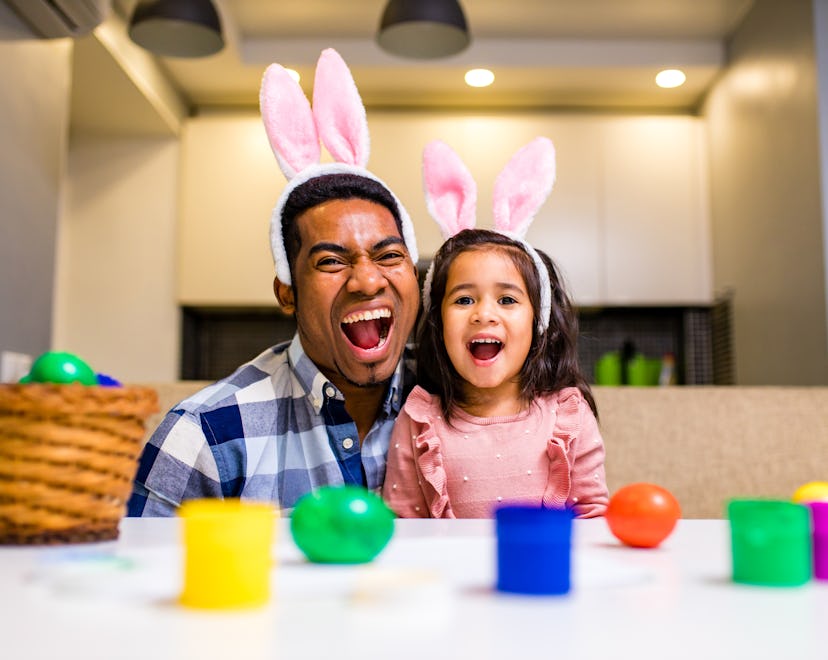 happy mixed race family celebrating Easter, painting eggs with brush smiling and laughing