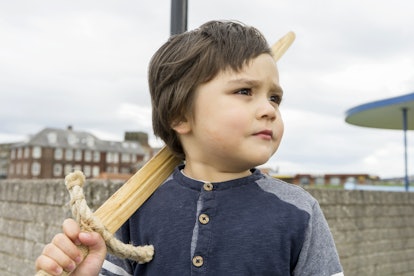 A toddler holding a wooden sword, staring into the distance.