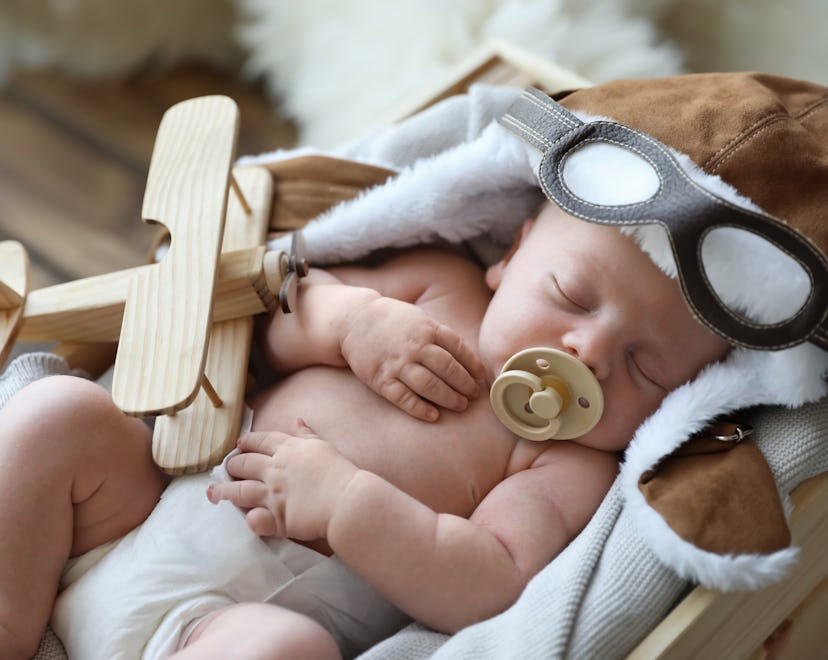 Cute newborn baby wearing aviator hat with toy sleeping in wooden crate
