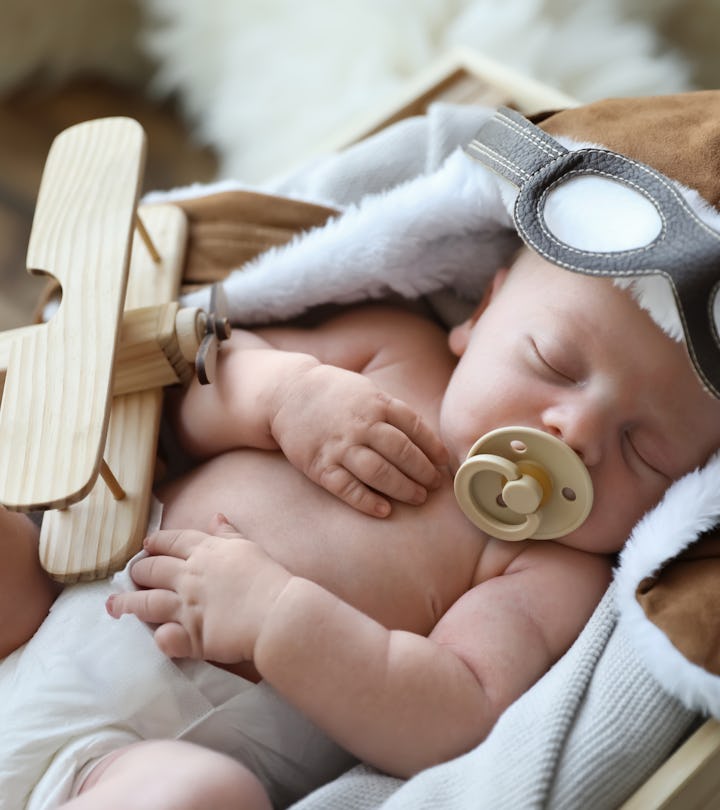 Cute newborn baby wearing aviator hat with toy sleeping in wooden crate