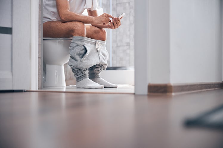 A man on his cell phone sitting on the toilet.