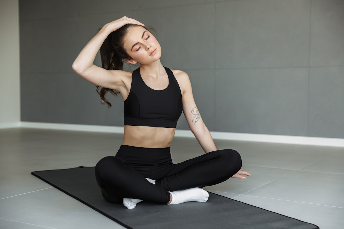 Photo of focused young woman in sportswear stretching her neck while working out on mat