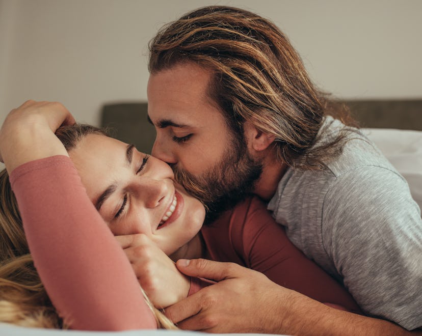 Man kissing his wife while sleeping on bed. Couple in bed covered in blanket with man kissing his pa...