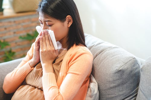 Asian pregnant woman sneezing she use tissue to cover her nose in article about using flonase during...