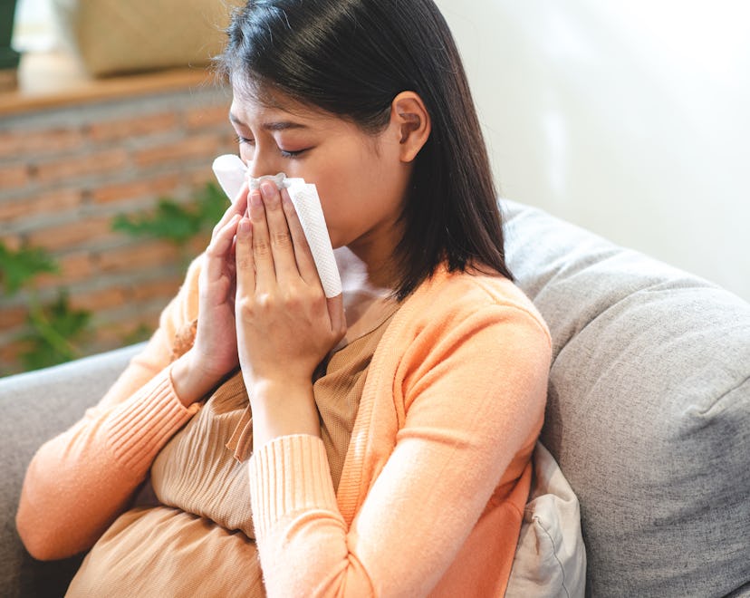 Asian pregnant woman sneezing she use tissue to cover her nose in article about using flonase during...