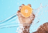 Water splash, orange in hand and studio background in healthy, vegan and nutrition food advertising,...