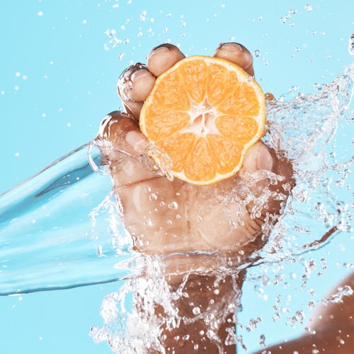 Water splash, orange in hand and studio background in healthy, vegan and nutrition food advertising,...