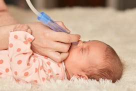Faceless mother using nasal aspiration sucks the snot from baby, child lying on bed on fluffy blanke...