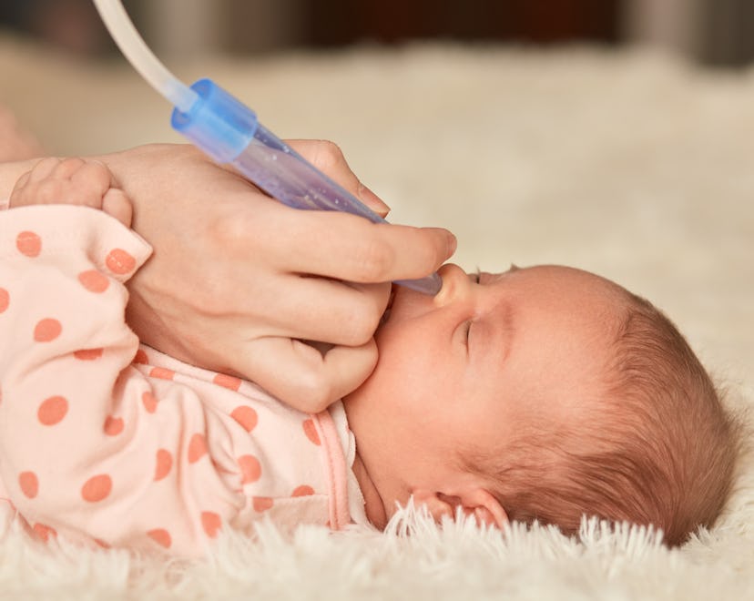 Faceless mother using nasal aspiration sucks the snot from baby, child lying on bed on fluffy blanke...