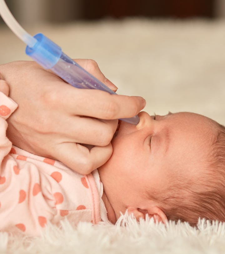 Faceless mother using nasal aspiration sucks the snot from baby, child lying on bed on fluffy blanke...