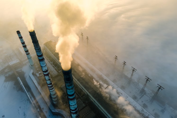 Aerial view of coal power plant high pipes with black smoke moving up polluting atmosphere at sunris...