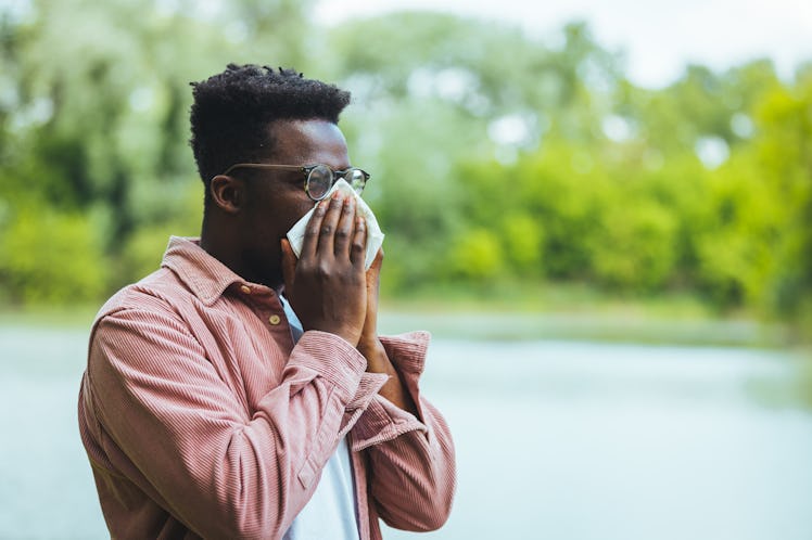A Black man sneezes into a tissue while green trees are behind him. What are the worst cities for se...