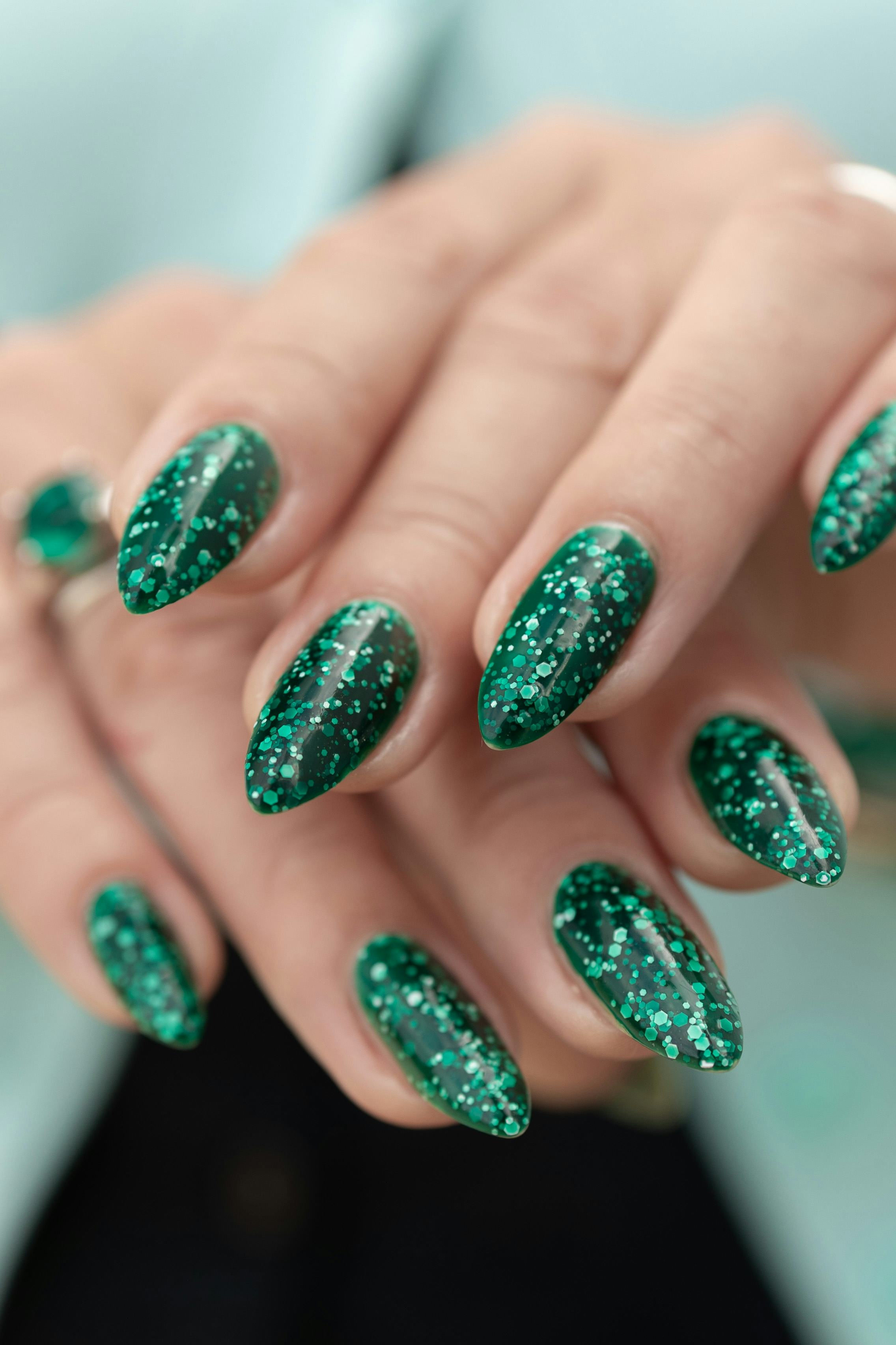 Woman's hand with long nails and green manicure with bottles of nail polish