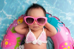 Nine day old newborn baby girl wearing pink sunglasses and a pink and white bikini. She is sleeping ...
