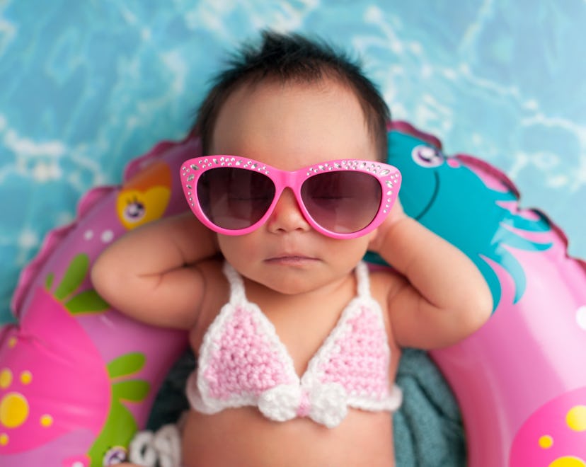 Nine day old newborn baby girl wearing pink sunglasses and a pink and white bikini. She is sleeping ...