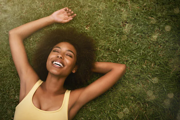 This is the life. Shot of a young woman laughing while relaxing on the grass.