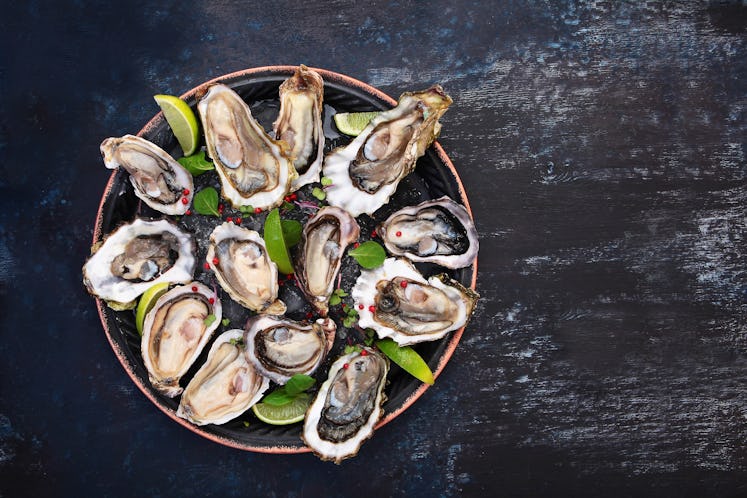 Fresh oysters with lime on a round plate. Oyster season. Seafood dish on a blue background. Oyster o...