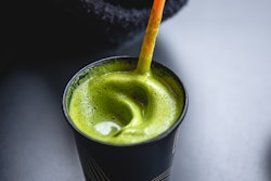 Delicious green matcha tea in a black cup close-up.