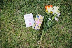 Bunch of flowers, gift and dedication card resting on a lawn for Mother's Day