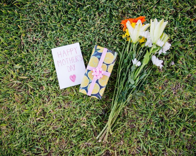 Bunch of flowers, gift and dedication card resting on a lawn for Mother's Day