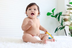 Portrait of smiling crawling baby sits on fluffy white rug, little cute kid girl playing with develo...