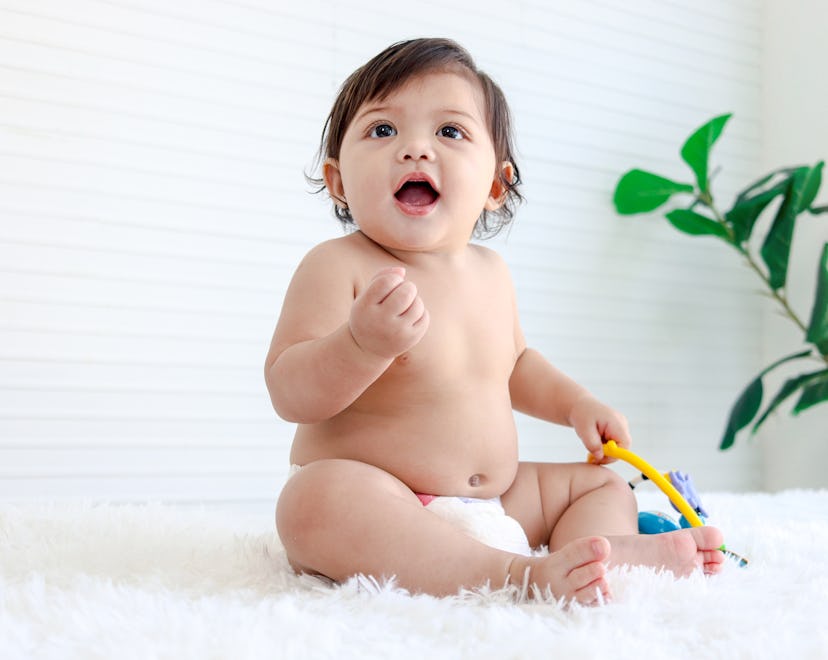 Portrait of smiling crawling baby sits on fluffy white rug, little cute kid girl playing with develo...