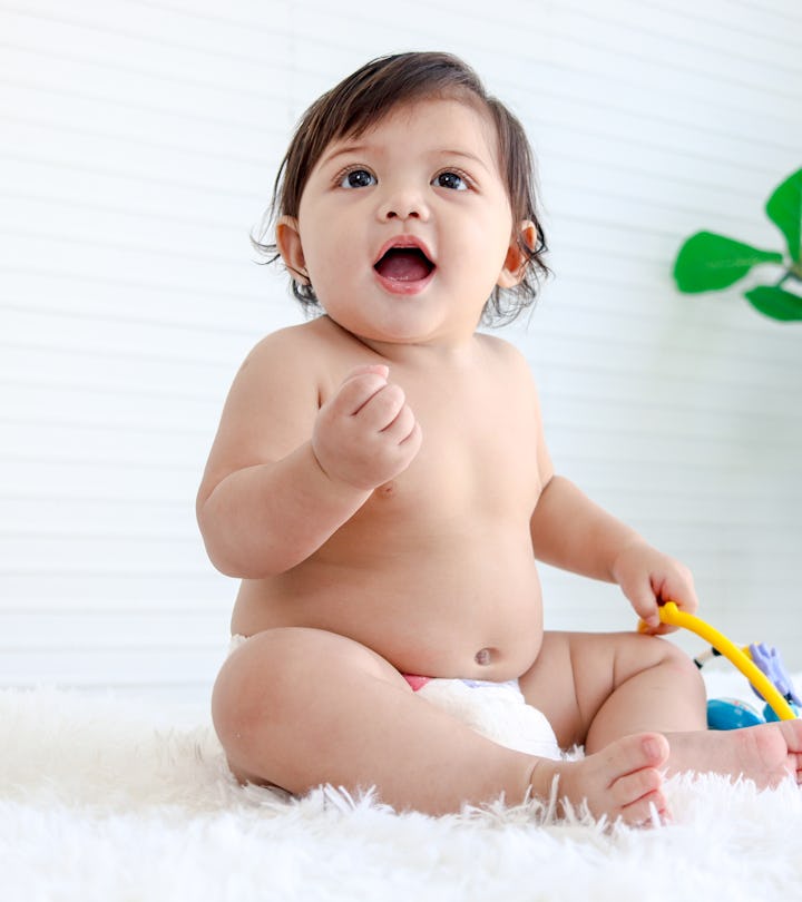 Portrait of smiling crawling baby sits on fluffy white rug, little cute kid girl playing with develo...