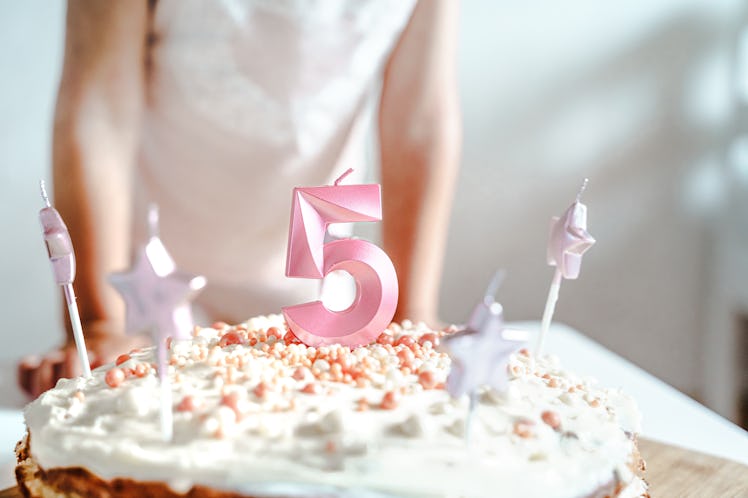 Big pink 5 number candle on homemade cake, with child standing behind it.
