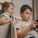 Little adorable brother and sister using smartphone, playing, watching cartoons together. Addicted t...