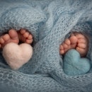 Legs, toes, feet and heels of newborn twins. Wrapped in a blue knitted blanket.  Knitted hearts of b...