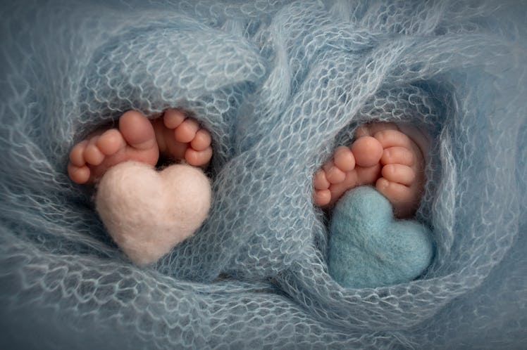 Legs, toes, feet and heels of newborn twins. Wrapped in a blue knitted blanket. Knitted hearts of b...