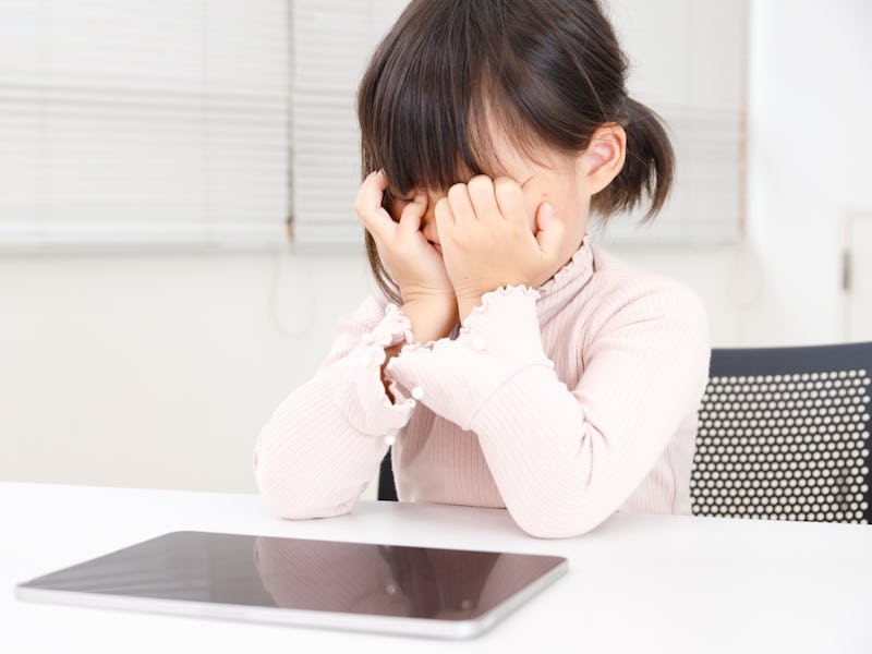 An Asian child whose eyes are tired from studying or playing games on a tablet. The child is rubbing...