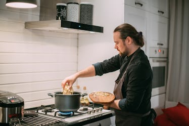 A man cooking with a pot on a gas stove in his kitchen.