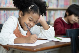 Portrait African american of smile little pupil writing at desk in classroom at the elementary schoo...