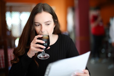 Serious woman drinking and reading menu sitting in a bar