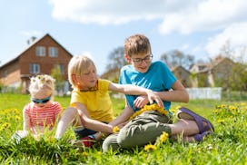 Children have fun in backyard of house on warm summer day. Brothers and sister sitting on the grass ...